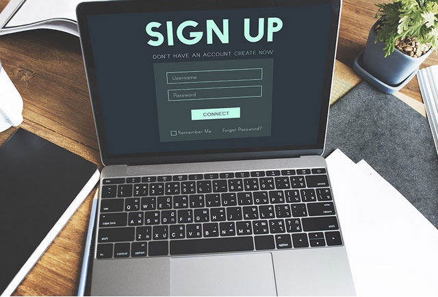 Wooden table with a notepad, pot plant and open laptop on a website's sign up page.