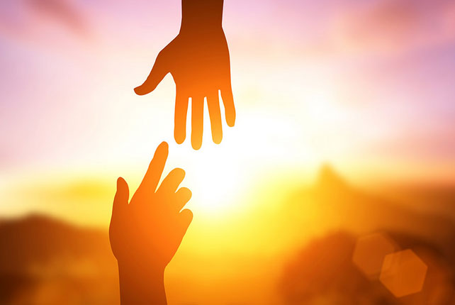 Two hands reaching for each other against the background of an orange sky.