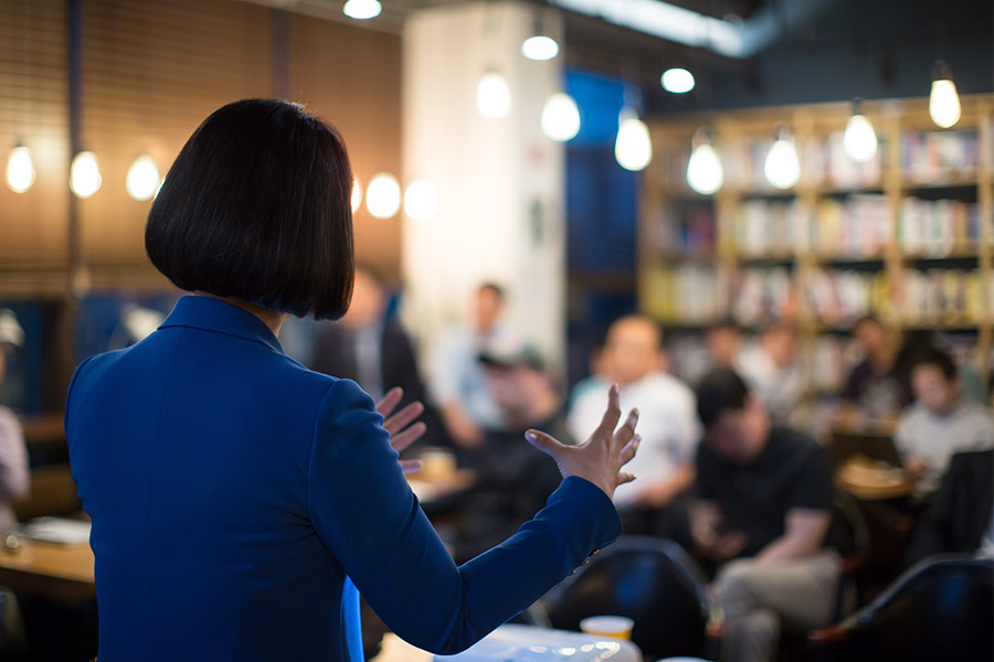 A woman in a blue suit addressing an audience.